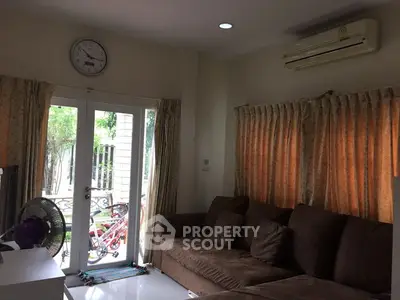Cozy living room with brown sofa and air conditioning, featuring natural light from glass doors.
