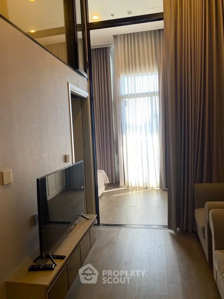 Modern living room with high ceilings and large windows, featuring elegant curtains and a sleek TV setup.