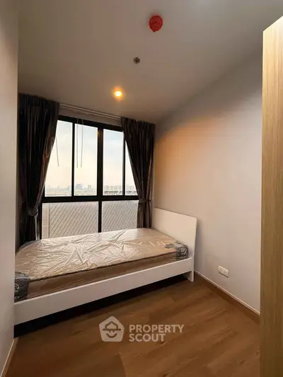 Cozy bedroom with large window offering city views, featuring a modern bed and wooden flooring.