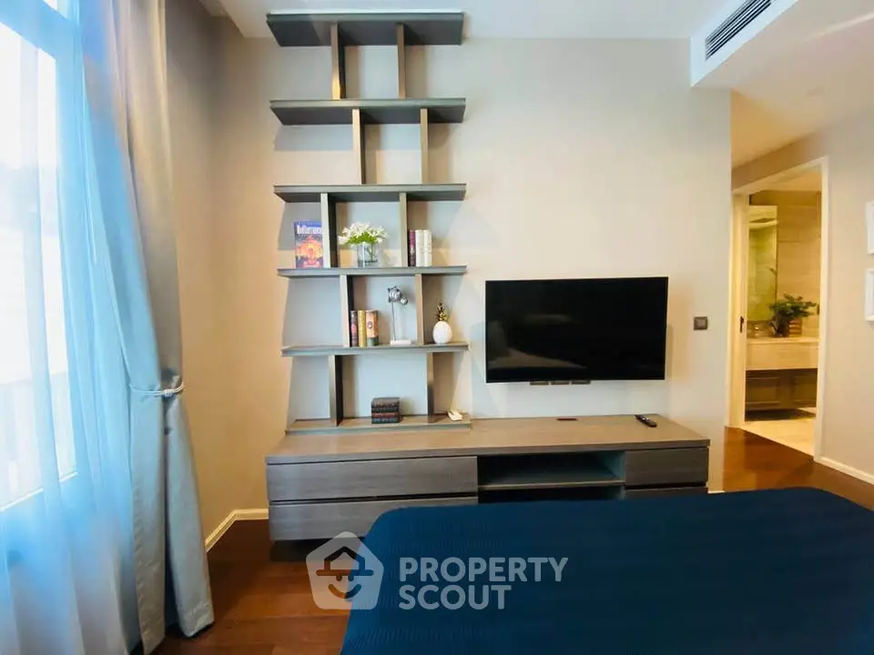 Modern bedroom with stylish shelving and wall-mounted TV, featuring elegant decor and natural light.