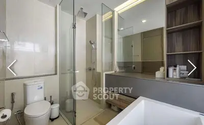 Modern bathroom with glass shower, sleek vanity, and bathtub in contemporary apartment.