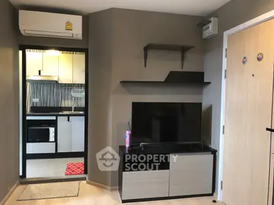 Modern living room with sleek TV stand and view into compact kitchen with appliances.