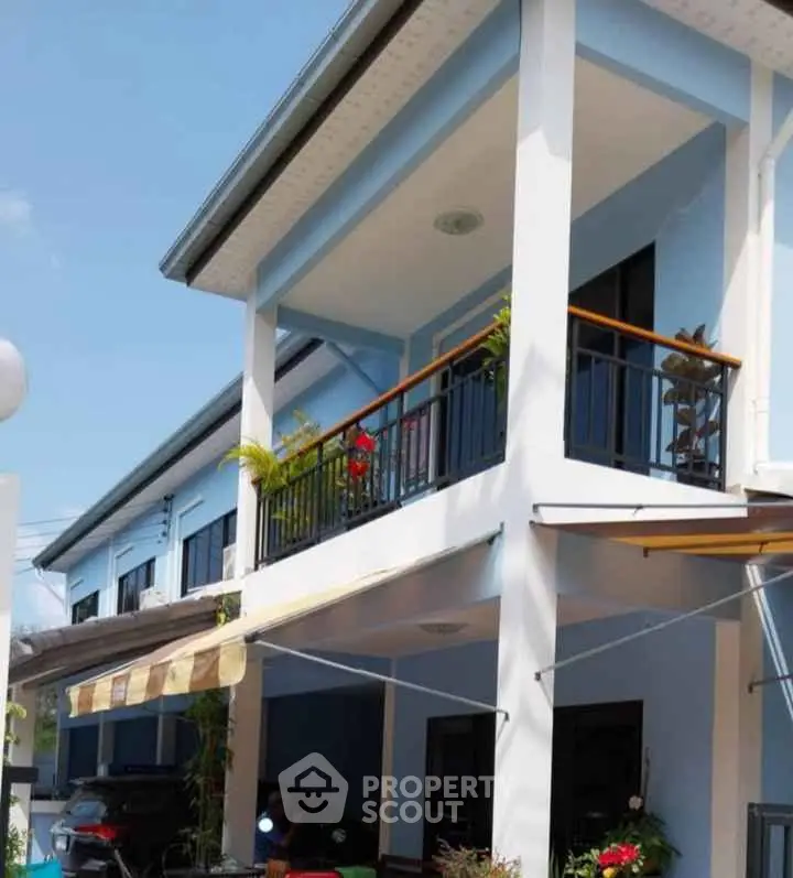 Charming two-story blue house with balcony and carport, perfect for family living.
