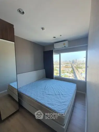 Cozy bedroom with a large window offering panoramic city views, modern furnishings, and ample natural light, perfect for urban living.