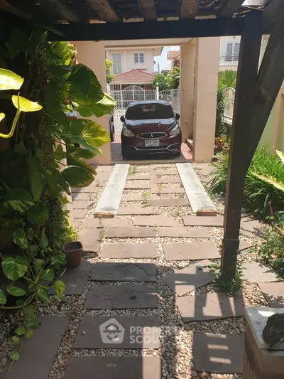 Charming garden pathway leading to a secure parking area with lush greenery and modern vehicle.
