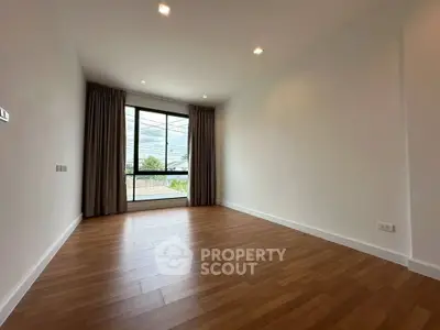 Spacious empty room with large window and wooden flooring, perfect for customization.