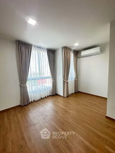 Spacious empty room with wooden flooring and large windows, perfect for customization.