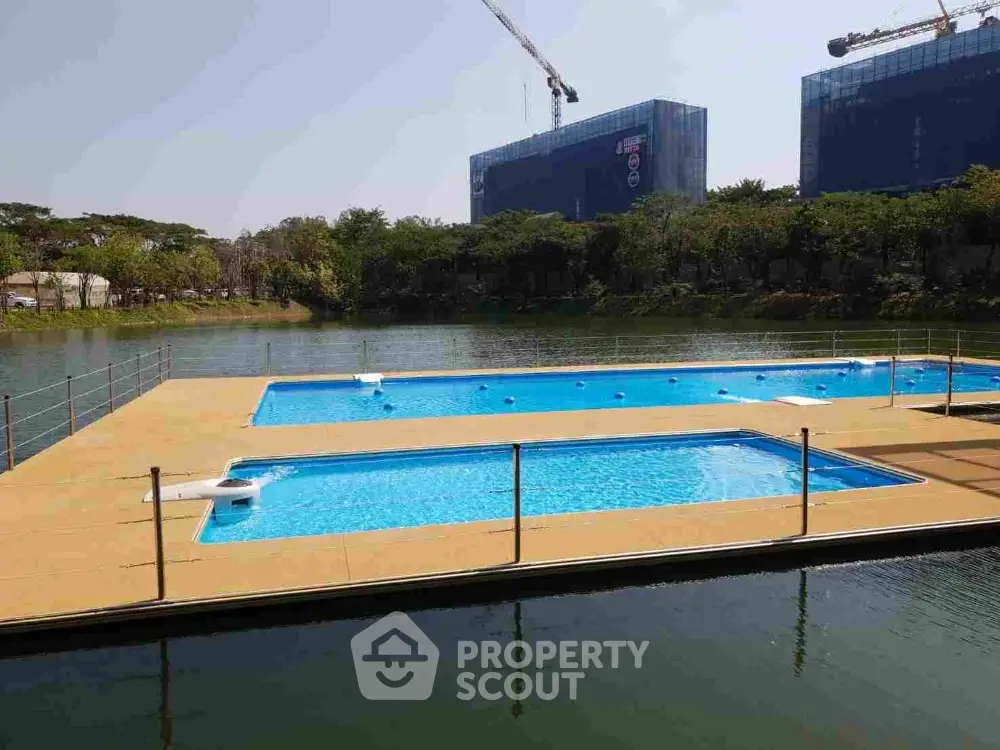 Luxurious outdoor swimming pool with crystal clear water, surrounded by a serene lake and modern high-rise buildings, offering an oasis of relaxation in a bustling cityscape.