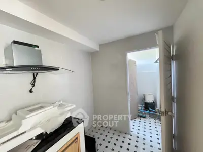 Compact kitchen with modern range hood and tiled flooring in a cozy apartment.