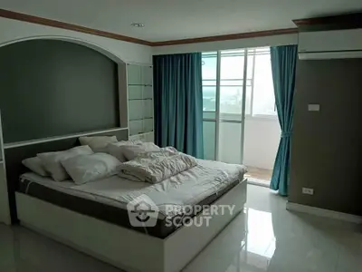 Spacious bedroom with balcony and modern decor in a high-rise apartment.