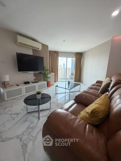 Spacious living room with modern decor and city view balcony, featuring a large TV and comfortable seating.
