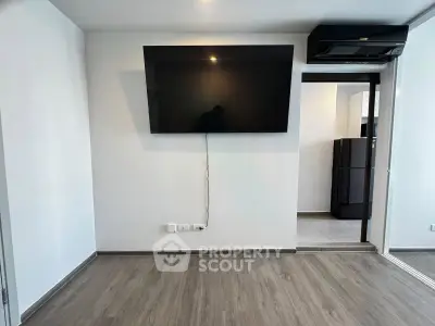 Modern living room with wall-mounted TV and sleek flooring, adjacent to kitchen area.