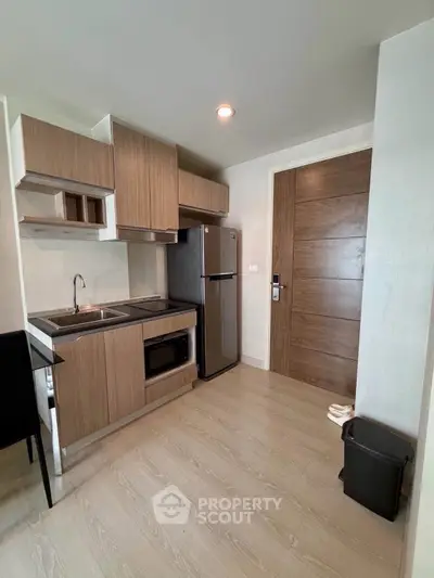 Modern compact kitchen with sleek wooden cabinets and stainless steel appliances in a stylish apartment.