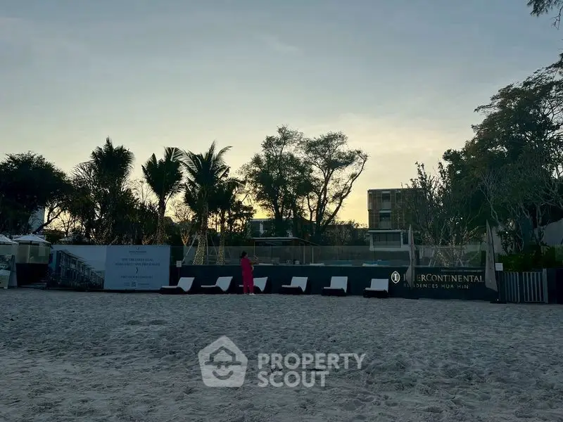 Beachfront property with lounge chairs and tropical trees at sunset.