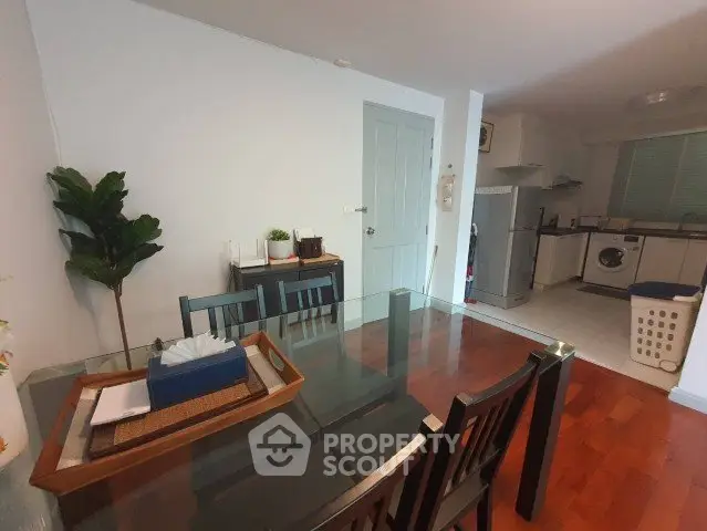 Spacious dining area with glass table and modern kitchen appliances in cozy apartment.