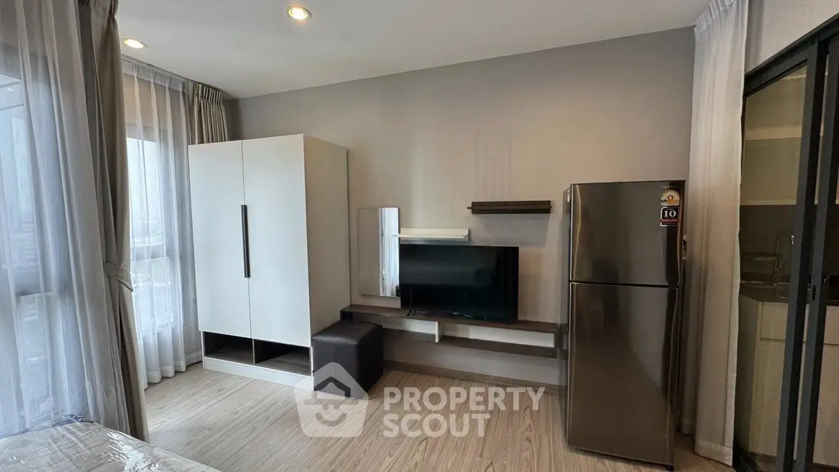 Modern living room with sleek furniture and large window, featuring a stylish wardrobe and stainless steel fridge.