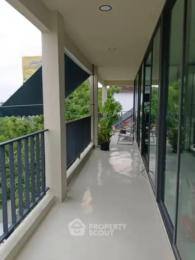 Spacious balcony with glass doors and lush greenery view, perfect for relaxation.