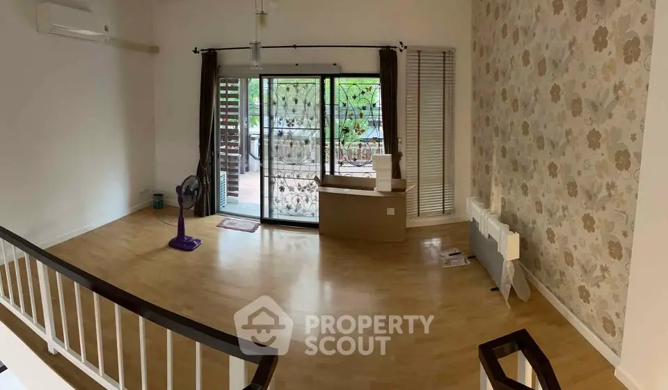 Spacious living room with wooden flooring and large windows opening to a balcony, perfect for natural light.
