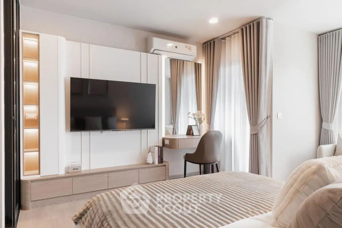 Modern bedroom with stylish decor and large TV, featuring elegant curtains and cozy bedding.