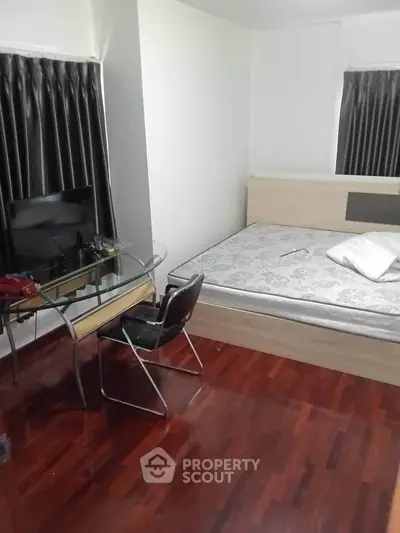 Cozy bedroom with wooden flooring, modern desk, and comfortable bed.