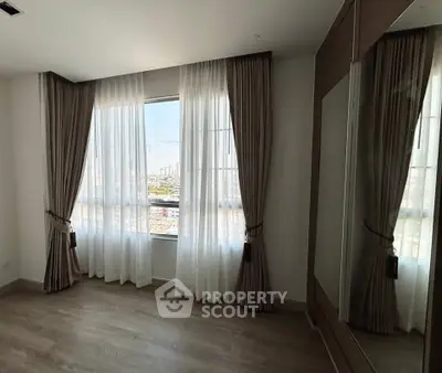Spacious bedroom with large window and elegant curtains offering city view