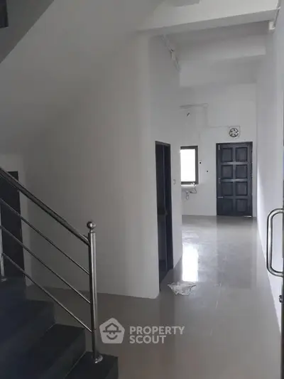 Modern hallway with sleek metal railing and glossy tiled floor, leading to a dark wooden door and window.