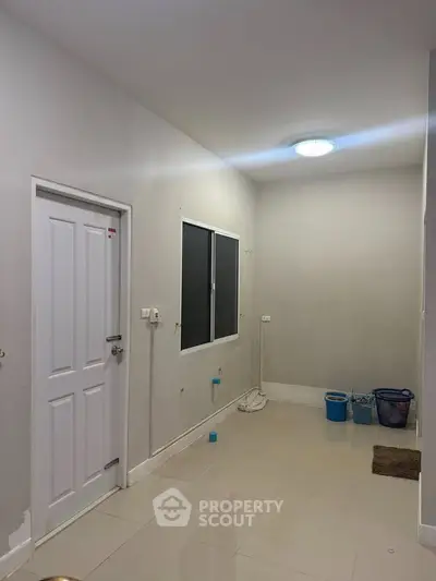 Minimalist interior space with white walls and tiled floor, featuring a door and window.