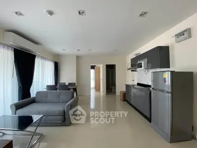 Modern open-plan living room with sleek kitchen, featuring large windows and contemporary furniture.
