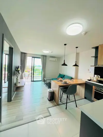 Modern open-plan living room with kitchen and balcony view, featuring stylish lighting and contemporary decor.