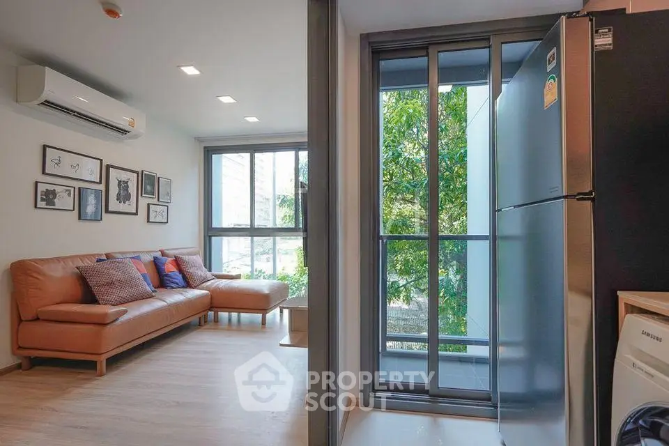 Modern living room with leather sofa and large windows next to a sleek kitchen area.