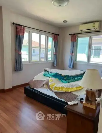 Cozy bedroom with large windows and wooden flooring, featuring an air conditioner and bedside lamp.