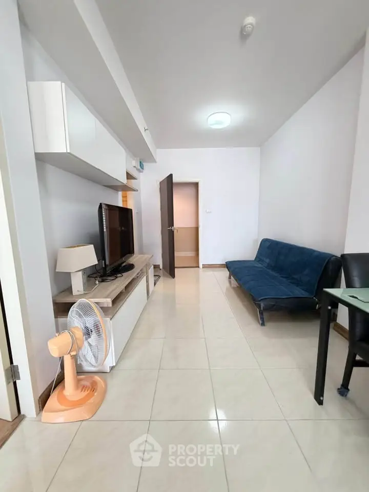 Modern living room with sleek furniture and tiled flooring, featuring a cozy blue sofa and flat-screen TV.