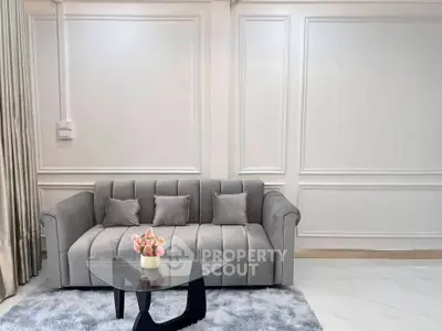 Elegant living room with plush gray sofa and modern glass coffee table on a soft rug.