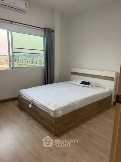 Modern bedroom with wooden flooring and large window offering natural light.