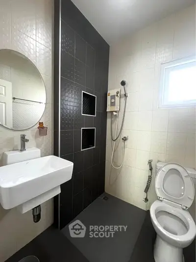 Modern bathroom with sleek black and white tiles, round mirror, and contemporary fixtures.