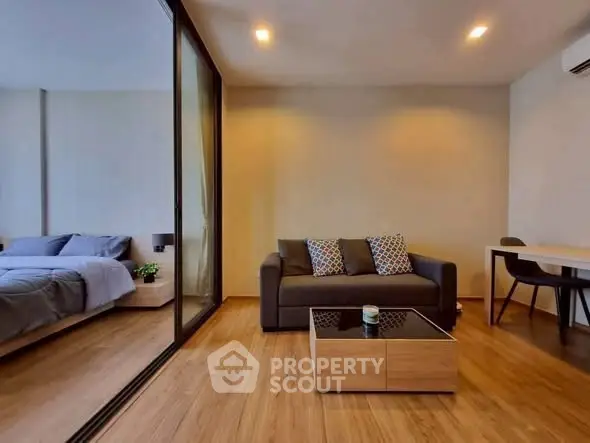 Modern living room with cozy sofa and stylish decor adjacent to a bedroom with glass partition.