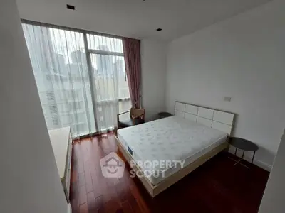 Spacious bedroom with large window and hardwood floors in modern apartment.