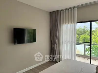 Modern bedroom with wall-mounted TV and large window overlooking greenery.