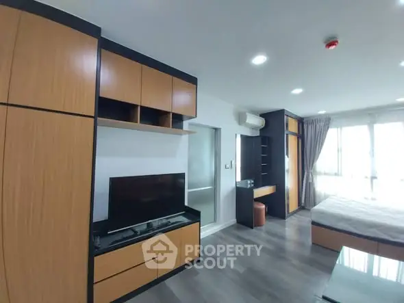 Modern studio apartment with sleek wooden cabinetry and large windows.