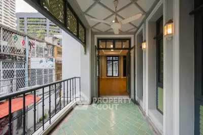 Charming balcony with green tiles and ceiling fan, leading to spacious interior with wooden flooring.