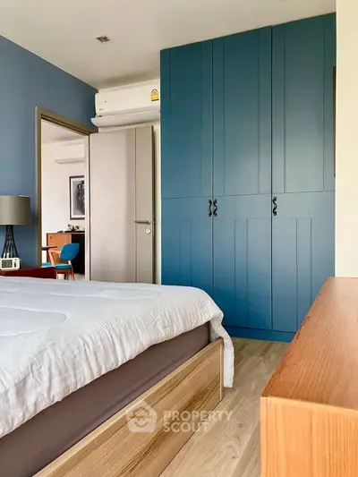 Modern bedroom with blue wardrobe and wooden accents, featuring a cozy bed and stylish decor.