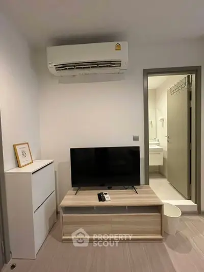 Modern living room with air conditioning and TV setup, leading to a bathroom.