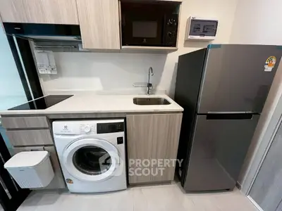 Modern kitchen with washing machine, microwave, and fridge in compact layout.