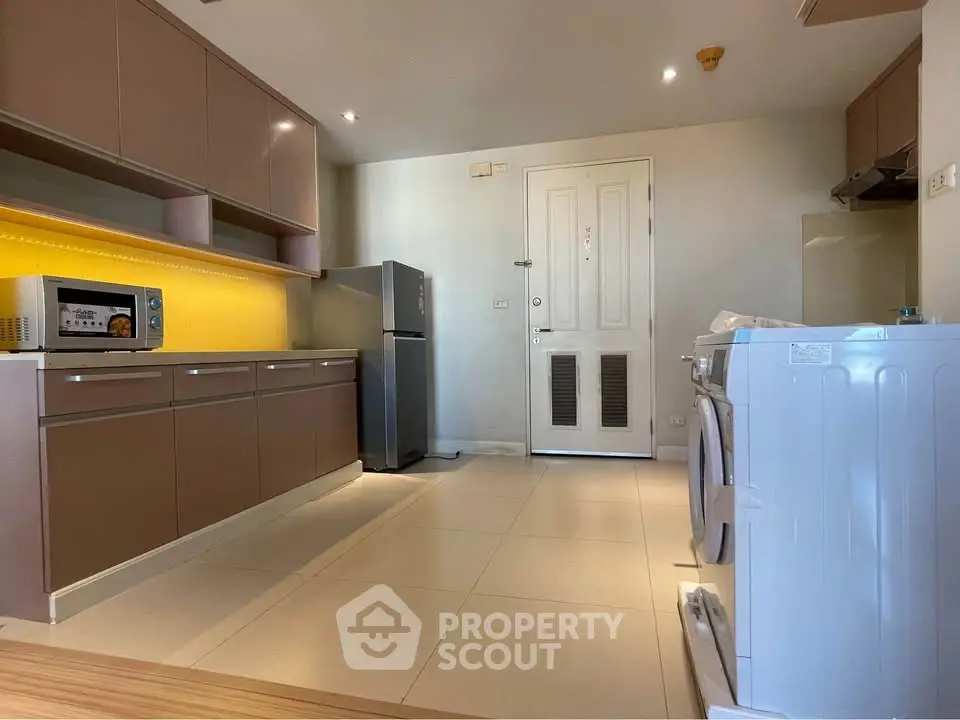 Modern kitchen with sleek cabinets, fridge, and washing machine in a spacious layout.
