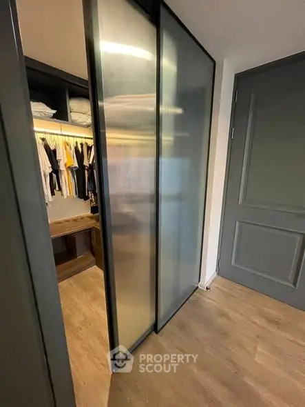 Modern walk-in closet with sliding glass doors and wooden flooring