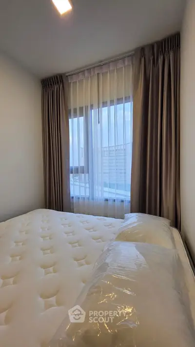 Cozy bedroom with plush mattress and elegant curtains, offering a serene ambiance and natural light.