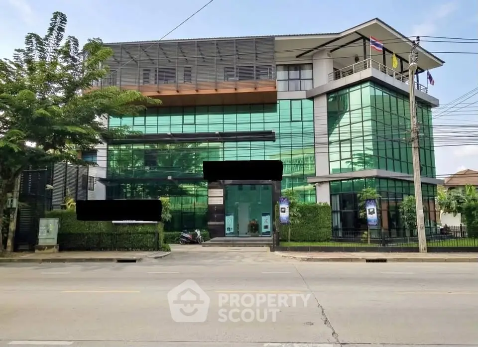 Modern glass-fronted commercial building with lush greenery and flags, ideal for business ventures.
