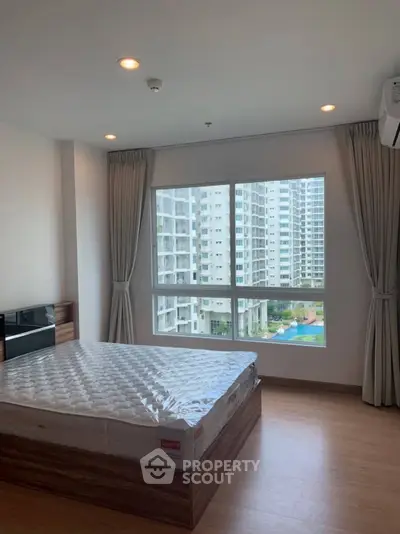 Spacious bedroom with large window offering stunning cityscape views in modern apartment.