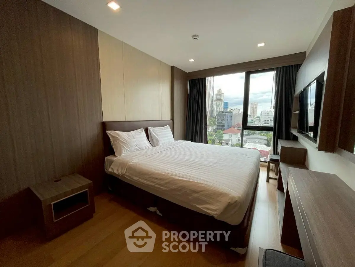 Modern bedroom with city view, featuring sleek wooden furniture and large windows.