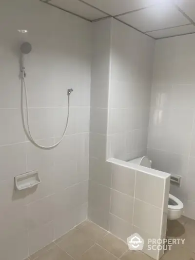 Pristine white-tiled bathroom featuring a full-size bathtub with overhead shower, a wall-mounted sink, and a modern toilet, all bathed in soft, ambient lighting.